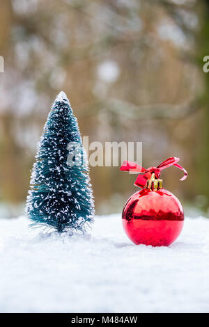 Petit arbre de Noël avec babiole rouge à l'extérieur dans la neige Banque D'Images