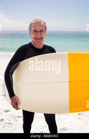 Portrait of senior man in wetsuit holding a surfboard Banque D'Images