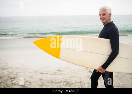 Portrait of senior man in wetsuit holding a surfboard Banque D'Images