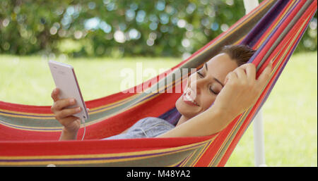 Happy young woman listening to music dans un hamac Banque D'Images