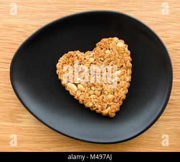 L'un des arachides en forme de coeur et d'avoine biscuit crêpes pour la Saint-Valentin sur plaque noire ovale sur table en bois. Banque D'Images