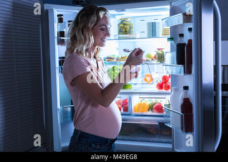 Young pregnant woman Eating Ice Cream Devant ouvrir Réfrigérateur Banque D'Images