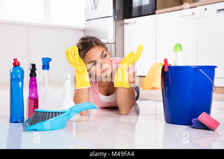 Sad Young Woman Lying On plancher de la cuisine et à l'équipement et les produits de nettoyage à Banque D'Images