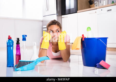 Sad Young Woman Lying On plancher de la cuisine et à l'équipement et les produits de nettoyage à Banque D'Images