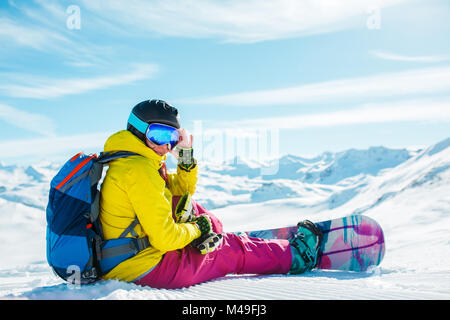 La photo d'une femme en casque avec sac à dos, assis sur la neige en snowboard Banque D'Images