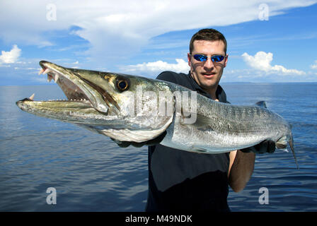 Heureux fisherman holding un magnifique baraccuda. La pêche en haute mer, pêche au gros, des prises de poissons. Banque D'Images