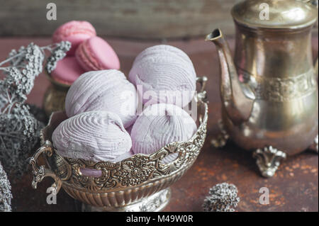 Des guimauves et macarons sur plaque de métal avec de petites fleurs blanches et de thé composition appareils sur fond de bois. Focus sélectif. Banque D'Images