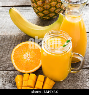 Smoothie et jus de fruits tropicaux : mangue, banane, orange dans un verre pot Mason sur le vieux fond de bois. Banque D'Images