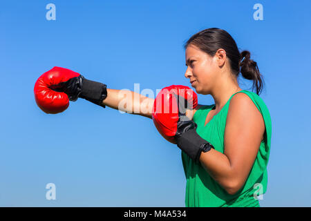 Jeune femme portant des gants de boxe rouge avec ciel bleu Banque D'Images