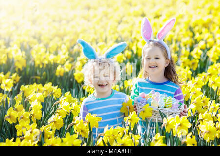 Chasse aux œufs de Pâques dans le jardin de printemps. Les enfants à la recherche d'oeufs colorés et des bonbons cachés dans le champ de fleurs en fleurs. Les enfants avec oreilles de lapin et panier d'oeufs Banque D'Images