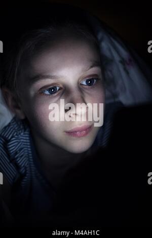 Girl Using Mobile Phone de se cacher sous une couette dans le lit la nuit Banque D'Images