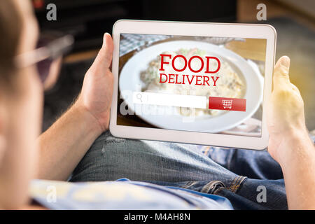 Livraison de nourriture app sur tablette. L'homme à l'aide de smart device à la maison à rendre une ordonnance de restaurant en ligne. Application imaginaire, site web et boutique internet Banque D'Images