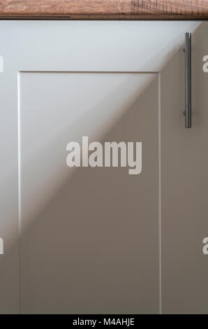 Partie d'une porte d'armoire de cuisine à la crème, avec poignée en inox, une ombre d'une fenêtre adjacente. Banque D'Images