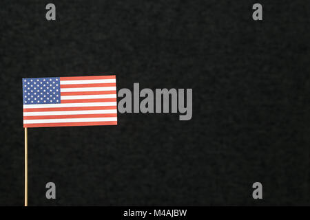 Le drapeau des États-Unis d'Amérique (USA) en papier sur bâtonnet de bois sur un fond sombre avec copie espace négatif pour le texte. Banque D'Images