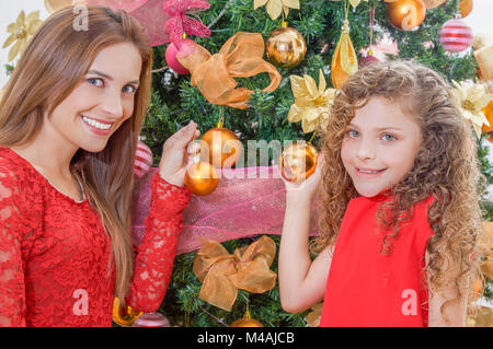 Close up of happy girl decorating Christmas Tree avec sa maman holding boules d'or, Noël en famille concept Banque D'Images