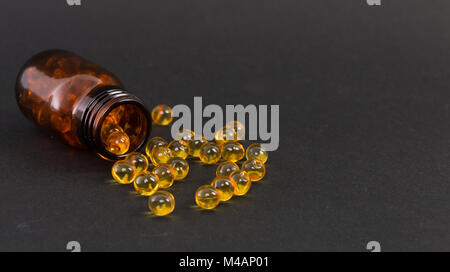 Jaune d'or renversé transparent capsules de vitamine sur fond sombre comme concept de traitement de la peau Banque D'Images