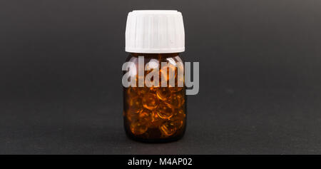 Bouteille pleine de capsules de vitamine e isolé sur fond noir comme l'huile de poisson pendant le déroulement du traitement de la peau Banque D'Images
