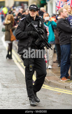 Agent de police armé d'un fusil et arme à la main à l'extérieur du château de Windsor dans le Berkshire. UK. Il marche derrière des soldats à relève de la garde. Banque D'Images