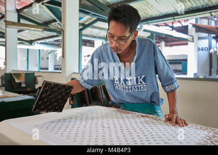 Batik Maker imprime de la cire chaude sur un chiffon avec un tampon de cuivre. Batik Winotosastro shop, Yogyakarta, Java, Indonésie. Banque D'Images