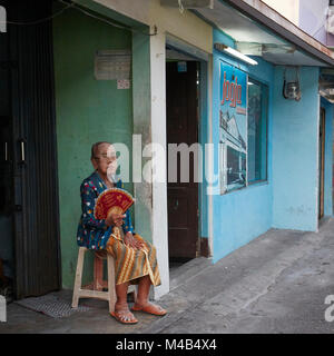 Habillé traditionnellement hauts femme est assise en face de sa boutique à Kampung Taman quartier. Yogyakarta, Java, Indonésie. Banque D'Images