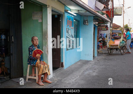 Habillé traditionnellement hauts femme est assise en face de sa boutique à Kampung Taman quartier. Yogyakarta, Java, Indonésie. Banque D'Images