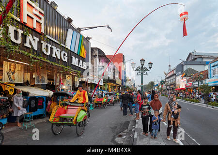 Pousse-pousse à vélo et les piétons sur la rue Malioboro au crépuscule. Yogyakarta, Java, Indonésie. Banque D'Images