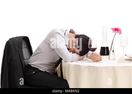 Ivre l'homme assis à une table de restaurant avec la tête vers le bas, isolé sur fond blanc Banque D'Images