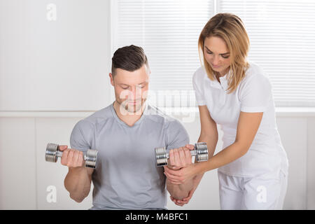 Young Female Physiothérapeute aide un homme à l'exercice avec haltères Banque D'Images