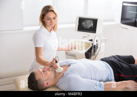 Jeune femme médecin effectuant l'échographie thyroïdienne test sur patient de sexe masculin Banque D'Images