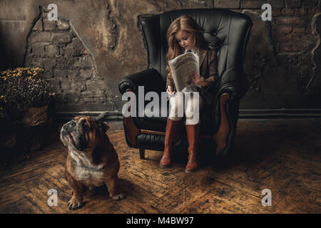 Fille de l'enfant dans l'image de Sherlock Holmes est assis dans un fauteuil et lit un journal à côté de bulldog Anglais sur fond de murs en briques anciennes et minable parque Banque D'Images