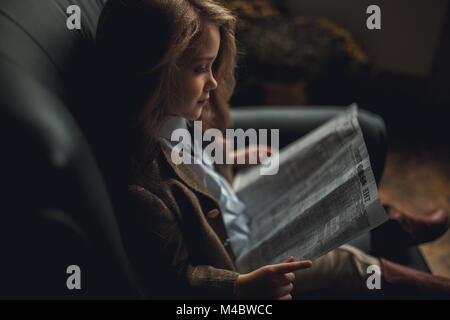 Fille de l'enfant dans l'image de Sherlock Holmes est assis dans un fauteuil et lit un journal. Close up. Banque D'Images