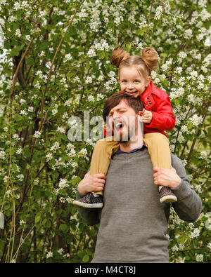 Le temps passé en famille. Le père détient sur ses épaules une petite fille dans un manteau de cuir. S'y greffent. Elle le tire par les oreilles. Marche de printemps Banque D'Images