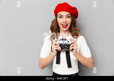 Portrait d'une jolie lycéenne habillés en uniforme holding photo caméra alors que l'article et à la caméra au fond de mur gris plus isolés Banque D'Images