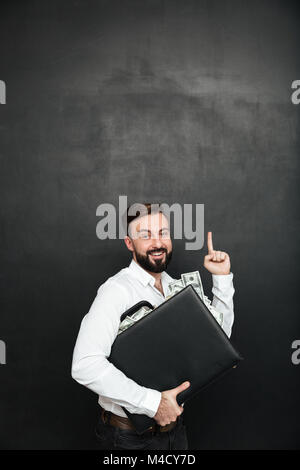 Photo de l'homme optimistes se réjouir son prix hugging noir porte-documents avec beaucoup d'argent comptant dollar vers le haut à l'intérieur gris foncé plus isolés backgrou Banque D'Images