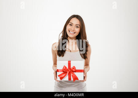 Photo de heureux woman holding fort d'un emballage-cadeau avec arc rouge d'être heureux et surpris d'obtenir cadeau d'anniversaire isolated over white background Banque D'Images