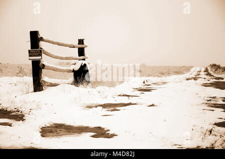 Un ancien pneu appuyé contre un poteau de clôture dans le désert de l'Utah patché avec la neige en sépia. Banque D'Images