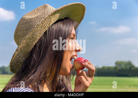 Woman with hat eating red apple à l'extérieur Banque D'Images