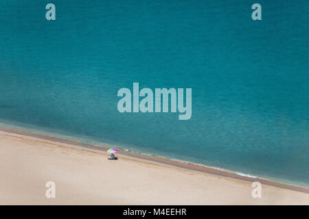 Femme âgée assise sur la plage sous un parasol, Waimea Bay, Oahu, Hawaii, États-Unis Banque D'Images