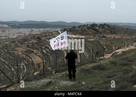 Un activiste de gauche se tient avec le drapeau du mouvement Peace Now et regarde l'avant-poste illégal du nativ Ha'avot officiellement une expansion de la colonie juive d'Elazar en Cisjordanie suite aux tentatives du gouvernement israélien de retarder le retrait de certaines des maisons de l'avant-poste malgré le Décision de la Cour suprême après avoir accepté la pétition d'un groupe de Palestiniens qui prétendaient que les maisons avaient été partiellement construites illégalement sur leurs terres. Israël Banque D'Images