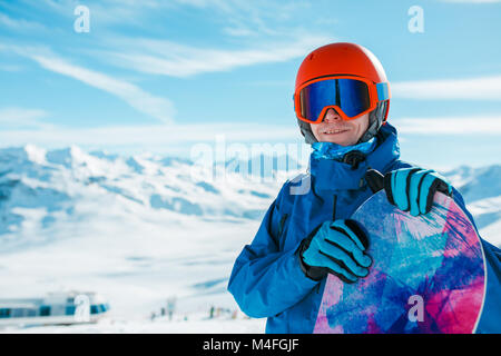 Image de l'homme sportif dans helmet looking at camera with snowboard sur fond de colline de neige pendant la journée Banque D'Images