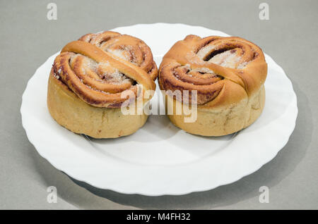 Deux petits pains à la cannelle sucrée de levure sur plaque blanche isolé sur le tableau gris. Banque D'Images