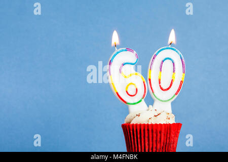 Numéro 60 anniversaire bougie dans un petit gâteau sur un fond bleu Banque D'Images