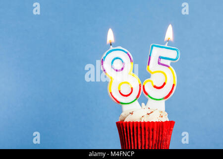 Numéro 85 anniversaire bougie dans un petit gâteau sur un fond bleu Banque D'Images