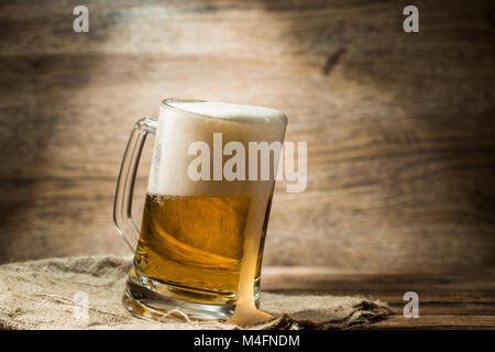 La bière mousseuse versée dans la tasse debout sur une table en bois Banque D'Images