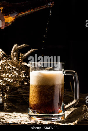 Bouteille de bière mousseuse versée dans la tasse vide sur fond de bois Banque D'Images