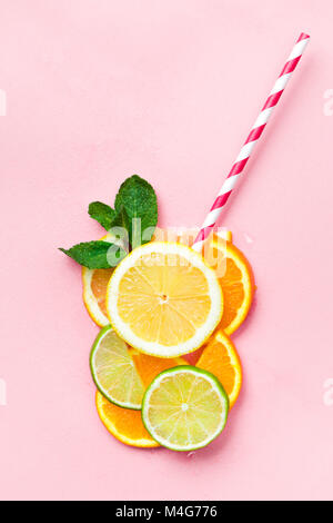 Verre de jus faits de rondelles d'agrumes avec des feuilles de menthe et d'une paille sur fond rose clair. Concept de jus d'agrumes Banque D'Images