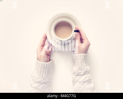 De haut en bas sur un fond blanc avec un bras de la jeune fille tenant une tasse de thé dans une tasse et soucoupe avec un swaeater cosy et chaleureux. Banque D'Images