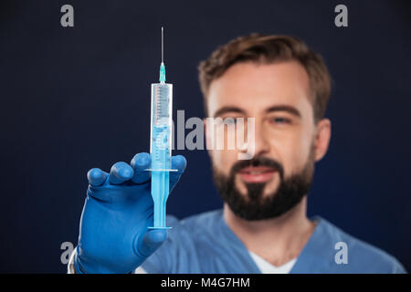 Portrait d'un homme médecin habillé en uniforme holding syringe isolated over fond sombre Banque D'Images