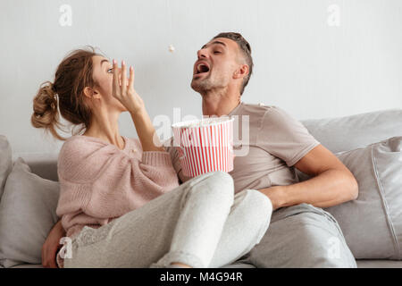 Amour ludique couple sitting on couch ensemble tout en s'amusant et en jouant avec le pop-corn Banque D'Images