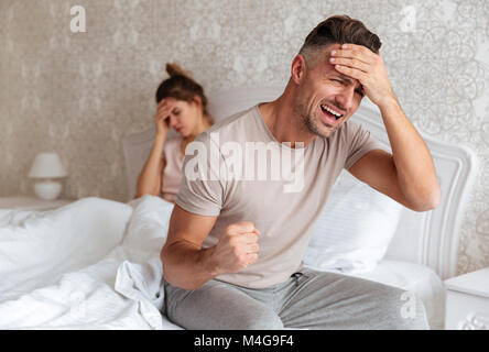 Confus inquiet homme assis sur le lit avec sa petite amie à la maison en arrière-plan Banque D'Images